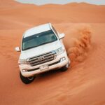 A Toyota Land Cruiser navigating a challenging desert dune, showcasing off-road capabilities.